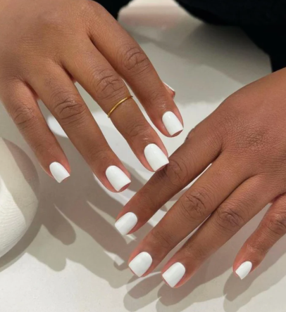 Minimalist white summer manicure with soft shadows, featuring a thin gold ring on one finger