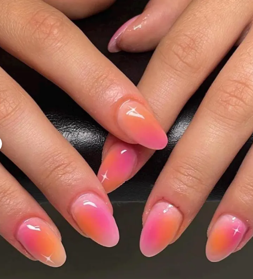 Close-up of glossy gradient nails transitioning from orange to pink, with white star accents on some nails.