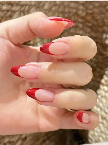 Close-up of a hand with long almond-shaped nails featuring a red half-moon design over a clear base.