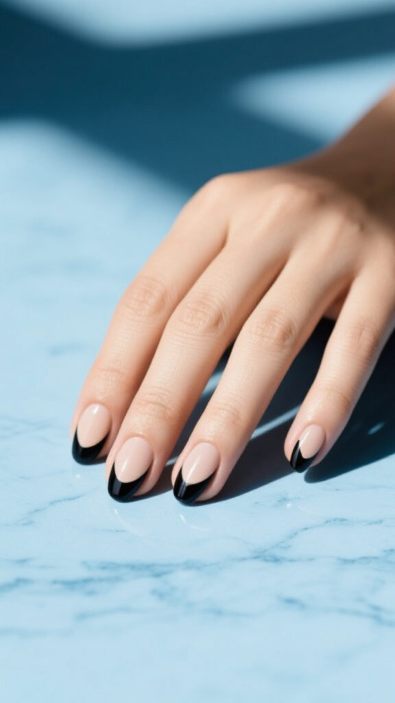 Nude base nails with sharp black French tips, modern twist on classic black nail design.
